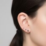 Zbliżenie na ucho z trzema kolczykami ułożonymi w rzędzie na płatku