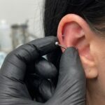 bliżenie na dłonie w czarnych rękawiczkach nitrylowych, które delikatnie, ale pewnie chwytają mały kolczyk