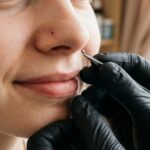 Dłonie w czarnych rękawiczkach nitrylowych delikatnie trzymają mały kolczyk