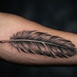 Kadr przedstawiający przedramię lubz niezwykle realistycznym, detalicznym tatuażem pojedynczego pióra