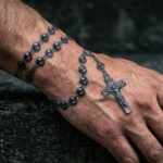 Detal na dłoń i nadgarstek mężczyzny, wokół których owinięty jest starannie wykonany tatuaż różańca w stylu realistycznym