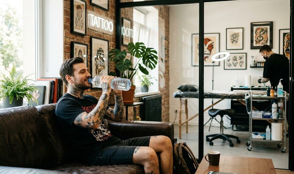 Kadr pokazujący wyluzowanego klienta siedzącego w poczekalni studia tatuażu.