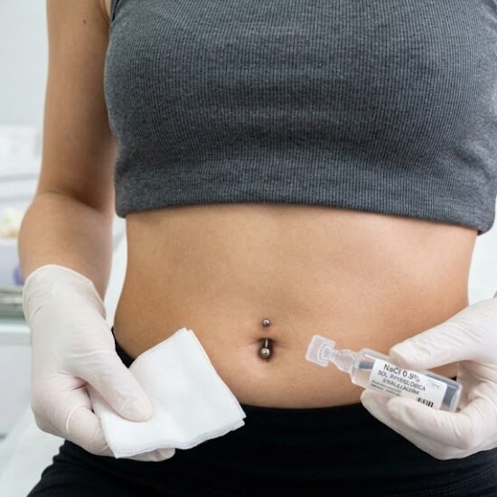 Kadr przedstawiający smukły brzuch z idealnie wykonanym, świeżym przekłuciem pępka