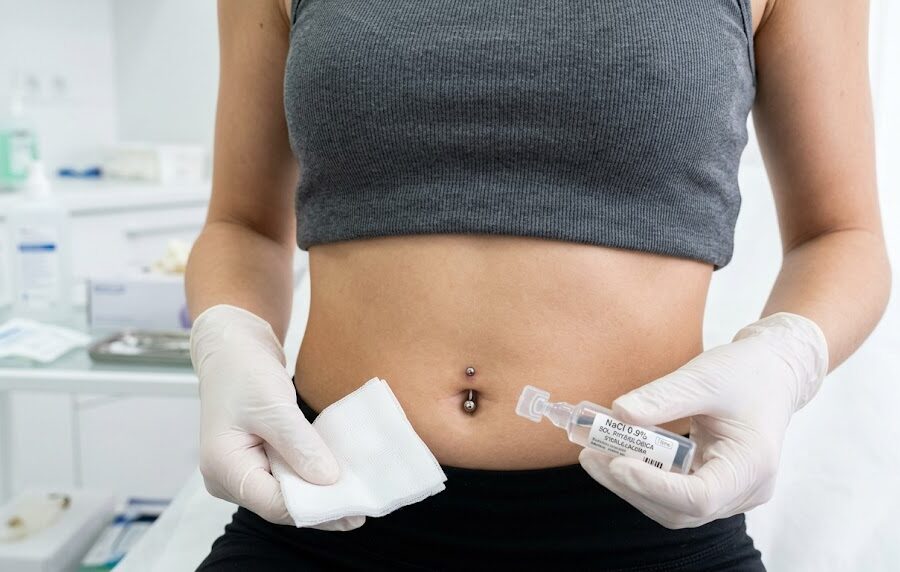 Kadr przedstawiający smukły brzuch z idealnie wykonanym, świeżym przekłuciem pępka