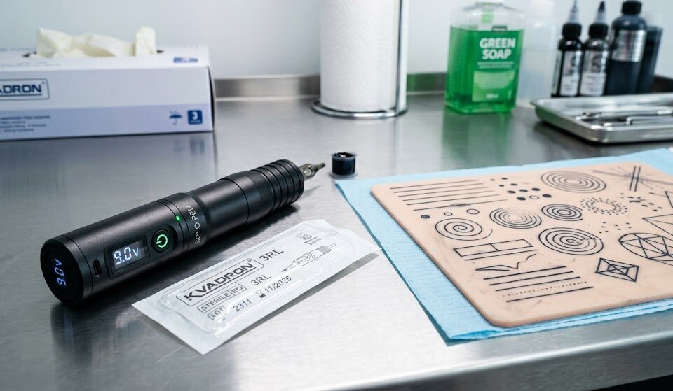 Na pierwszym planie leży nowoczesna, bezprzewodowa maszynka do tatuażu